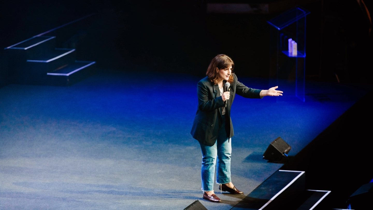 Ashley England emceeing the WeWork Summit at Madison Square Garden in 2019, microphone in hand, arm extended toward the audience